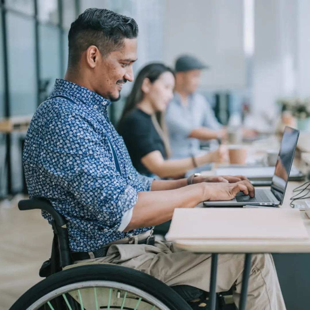 Persona usuaria de silla de ruedas trabajando en una laptop dentro de una oficina, representando inclusión, accesibilidad y oportunidades para el desarrollo profesional y financiero con Banamex.