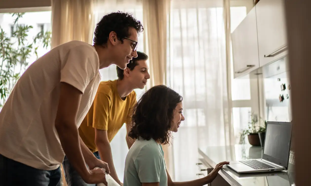 Tres personas revisan juntas una laptop sobre la barra de una cocina luminosa, programa de Educación Financiera Banamex