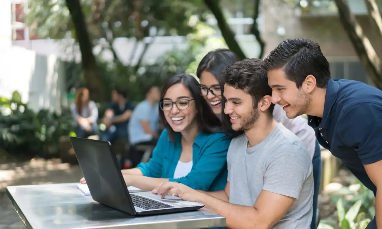 Jóvenes sonrientes trabajan en equipo frente a una laptop en un espacio luminoso, programa de Educación Financiera Banamex