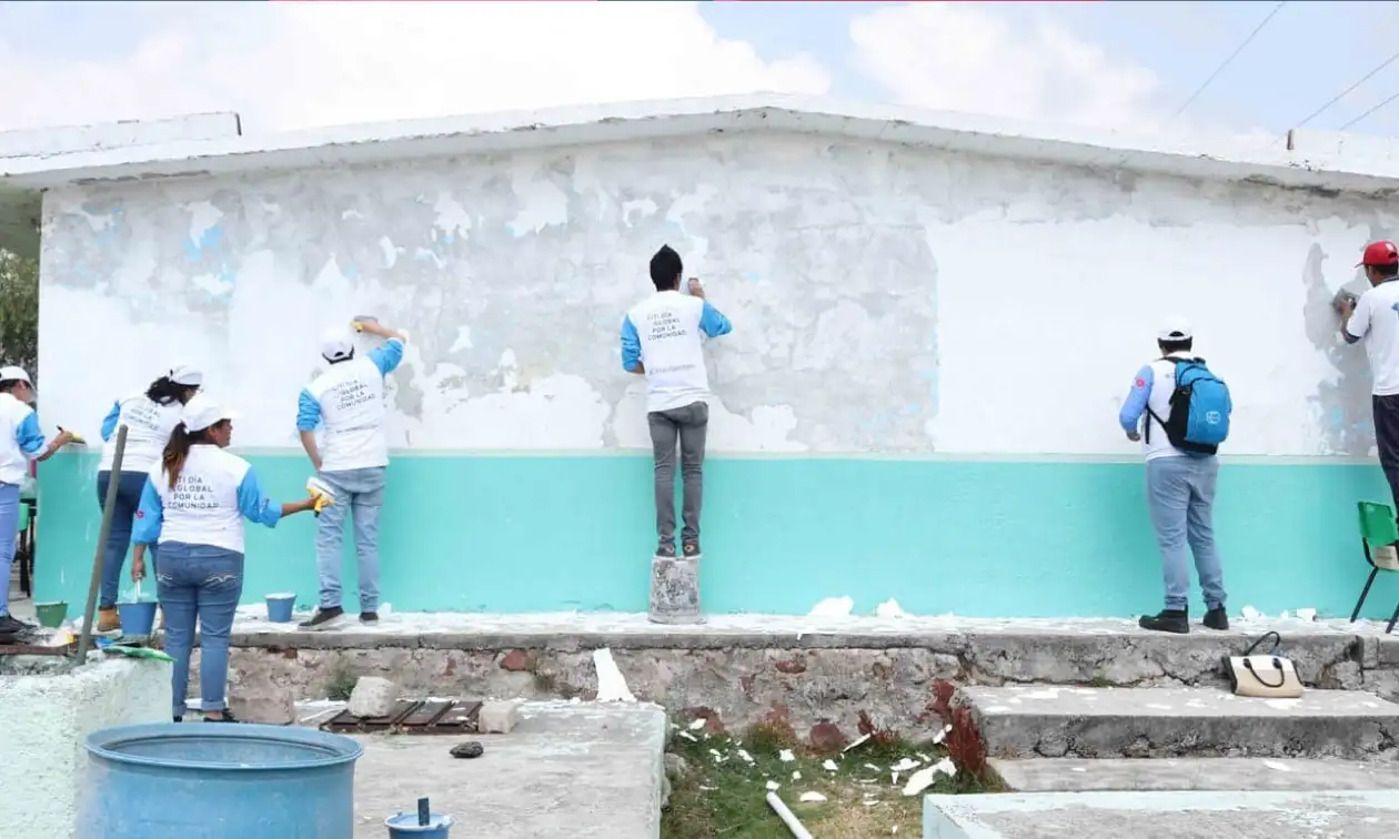 Voluntarios pintan un mural turquesa al aire libre durante una jornada de Voluntariado Banamex