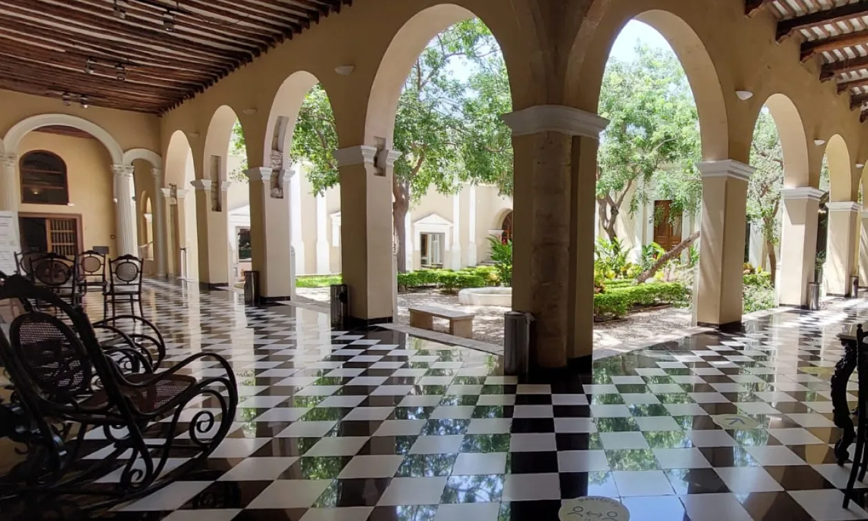 Galería de arcos con piso ajedrezado frente al patio arbolado de Casa Montejo, sede cultural de Banamex en Mérida
