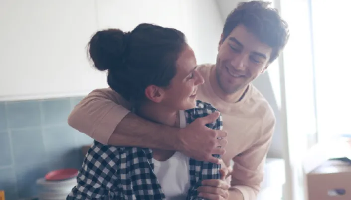 Pareja joven abrazándose y sonriendo en la cocina de casa, representando bienestar, unión familiar y la tranquilidad de construir un futuro seguro con Banamex.