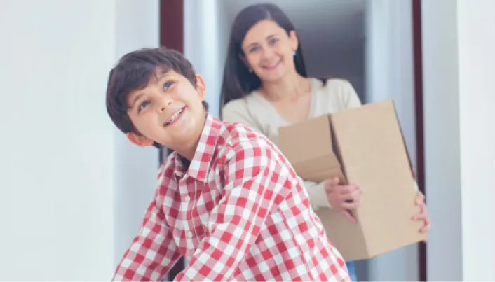 Madre e hijo sonrientes cargando cajas de mudanza al llegar a su nuevo hogar, representando la ilusión de comprar casa y el respaldo financiero de Banamex.