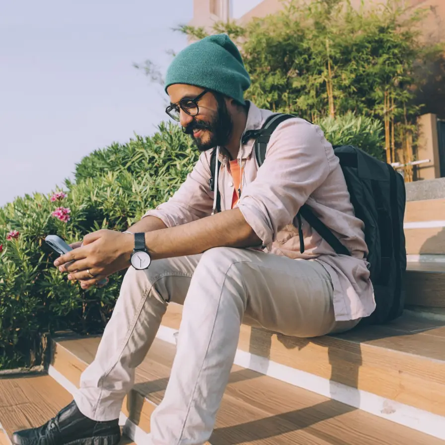 Hombre joven sonriente con gorro y mochila sentado al aire libre rodeado de vegetación, representando estilo de vida activo, bienestar y libertad financiera con Banamex.