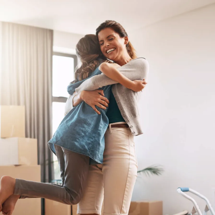 Pareja feliz abrazándose entre cajas de mudanza en su nuevo hogar, celebrando la ilusión de estrenar casa con el respaldo financiero de Banamex.
