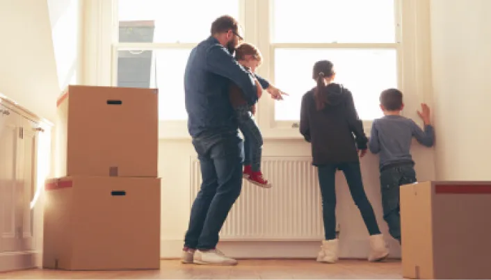 Familia con cajas de mudanza en una vivienda iluminada por luz natural, observando el interior de su nuevo hogar junto a una ventana.