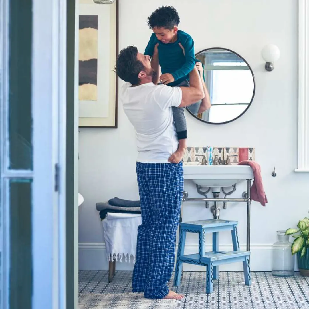 Persona levantando a un menor en un baño residencial, reflejando convivencia familiar y actividades cotidianas dentro del hogar.