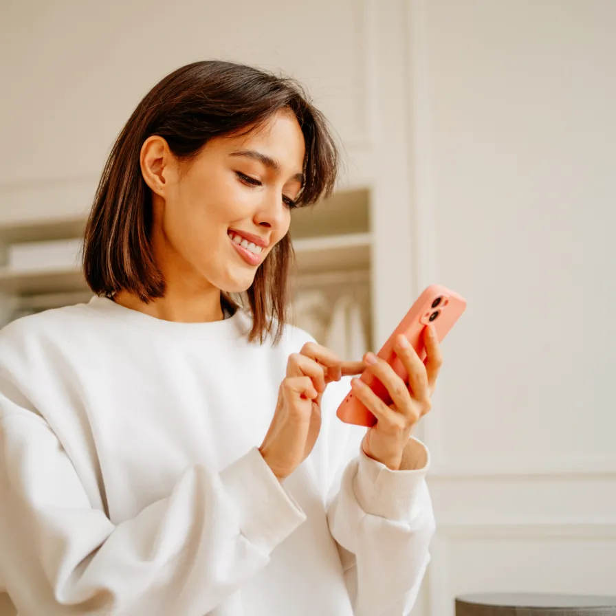 Persona utilizando un teléfono móvil en interiores, interactuando con una aplicación digital desde un dispositivo con funda color coral.