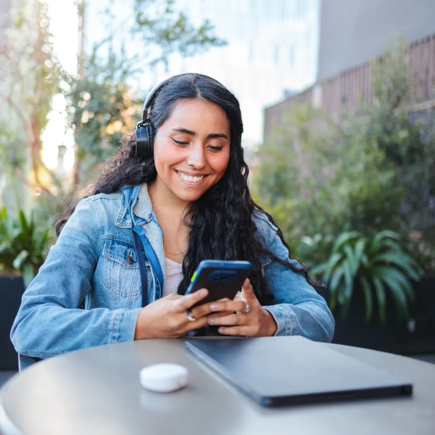 Persona usando un teléfono móvil y audífonos al aire libre, representando el acceso a servicios digitales y beneficios de Banamex.
