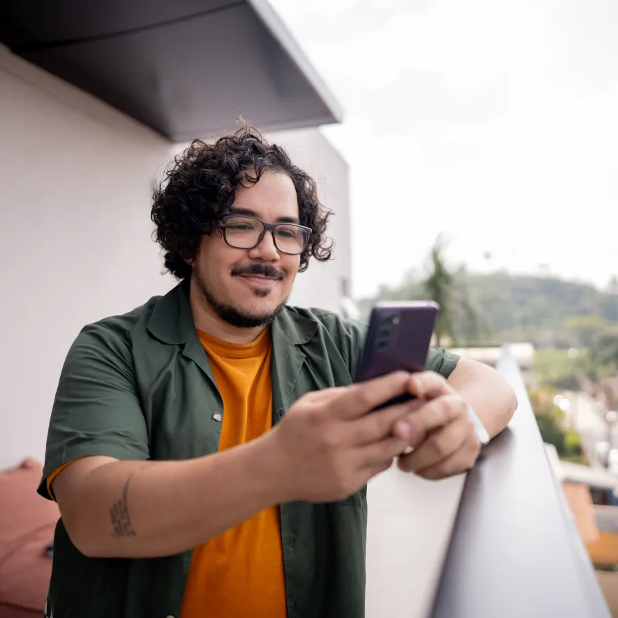 Persona utilizando un teléfono móvil desde un balcón, representando el acceso a servicios financieros digitales de Banamex Móvil.