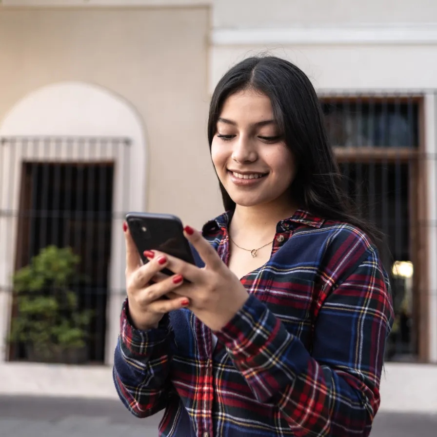 Persona usando un teléfono móvil al aire libre, representando el acceso rápido y seguro a servicios digitales de Banamex Móvil.