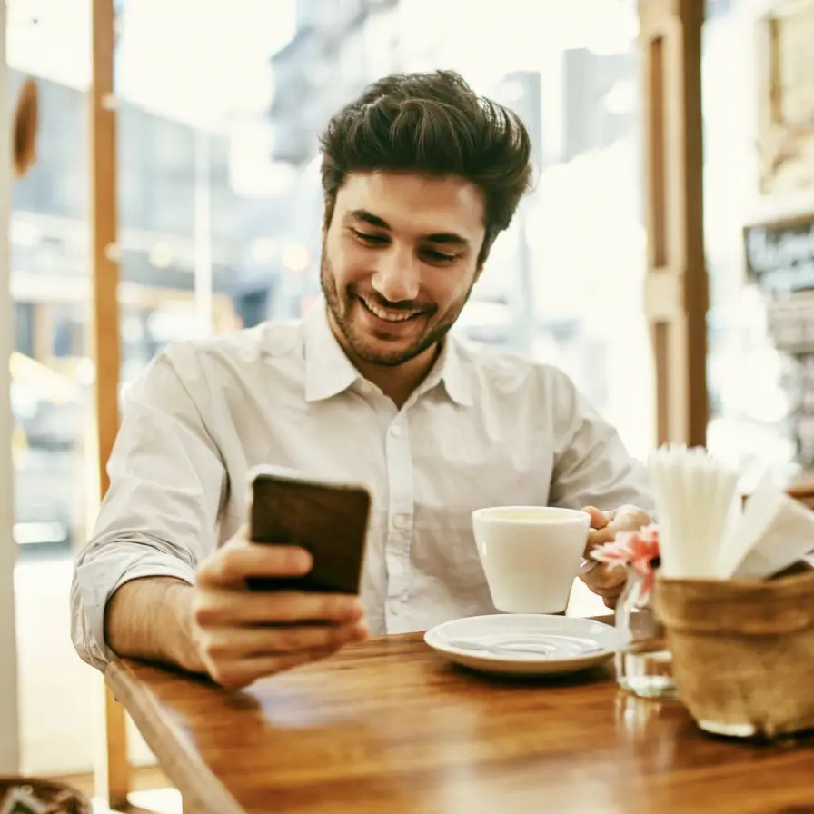 Persona revisando información desde un teléfono móvil en una cafetería, mientras gestiona servicios financieros y actividades digitales.