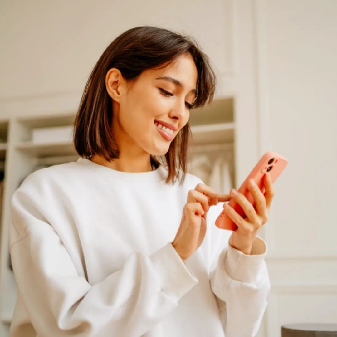 Persona utilizando un teléfono móvil desde casa para consultar información, realizar trámites y gestionar servicios digitales de manera sencilla.