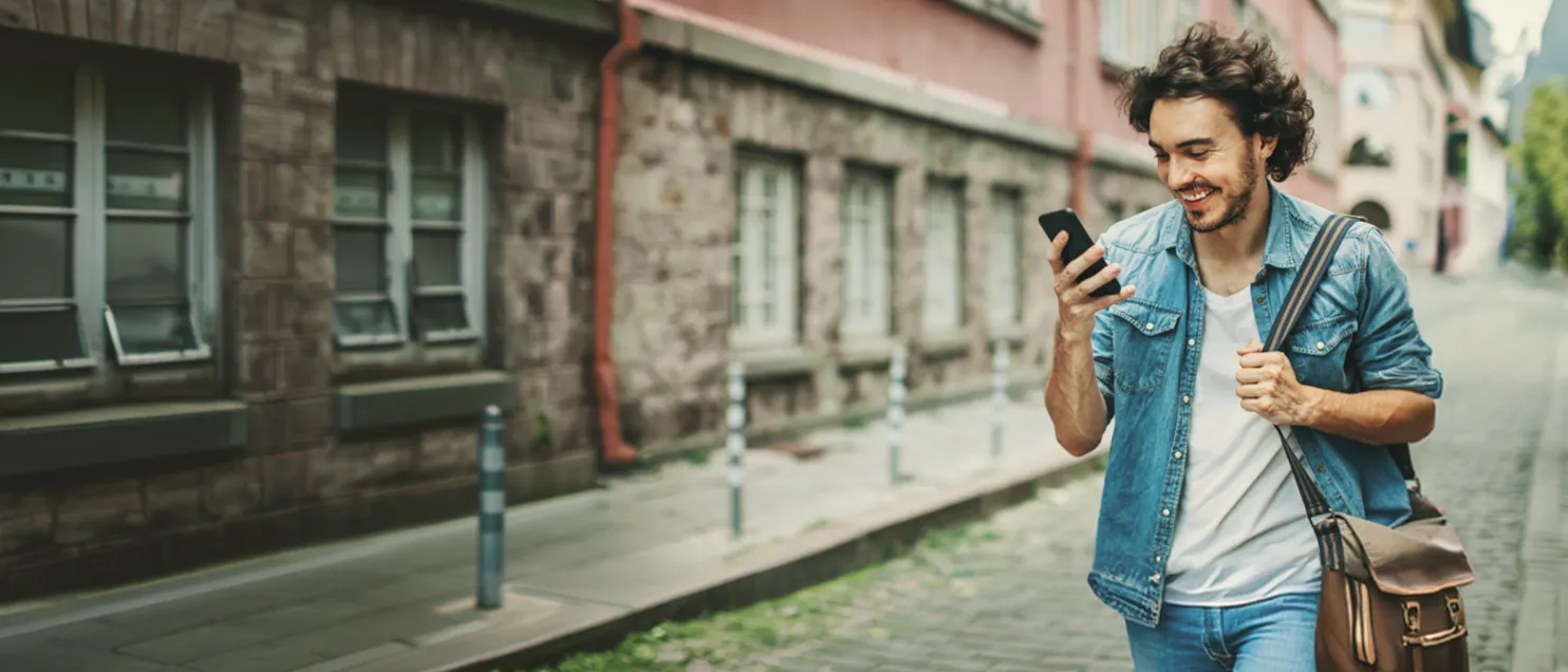 Persona consultando información desde un teléfono móvil mientras camina por una calle urbana, destacando movilidad y conectividad digital.