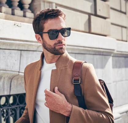 Persona con gafas de sol y bolso al hombro caminando en un entorno urbano, reflejando movilidad, estilo de vida y dinamismo.