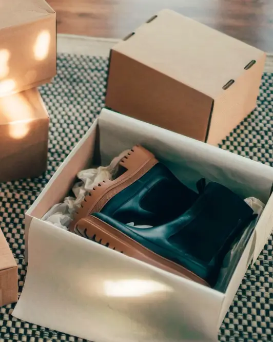 Caja abierta con botas nuevas y empaques de envío, representando compras en línea y beneficios de pago con tarjetas Banamex.