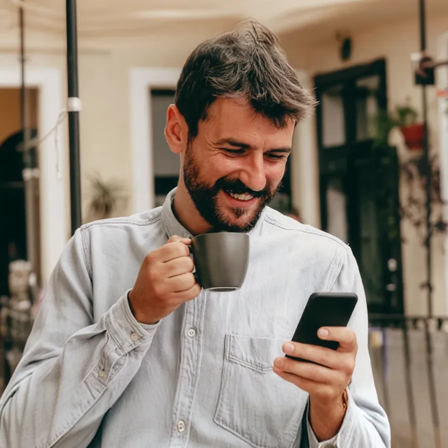 Persona tomando café mientras consulta un teléfono móvil, representando el acceso a promociones y servicios digitales de Banamex.