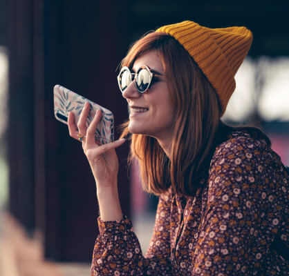 Persona utilizando un teléfono móvil para enviar un mensaje de voz, destacando conectividad, comunicación y servicios digitales en movimiento.