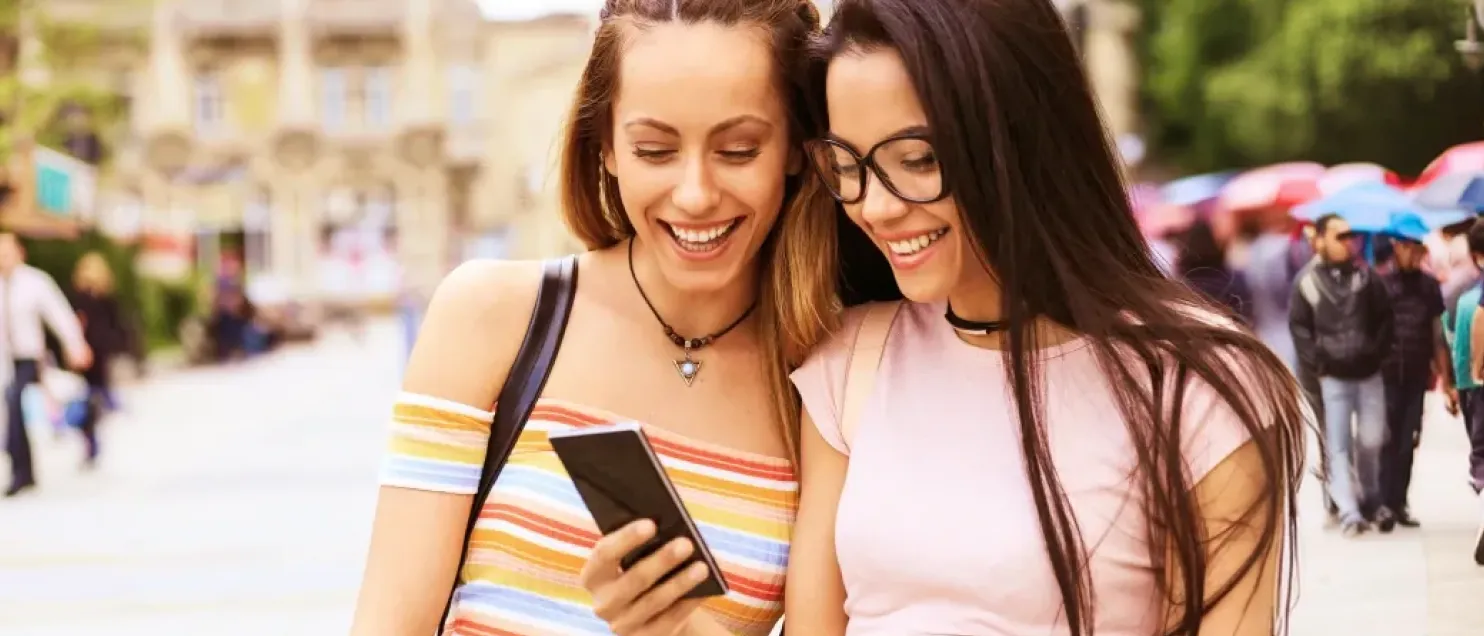 Personas consultando información en un teléfono móvil mientras recorren la ciudad, destacando conectividad, movilidad y servicios digitales.