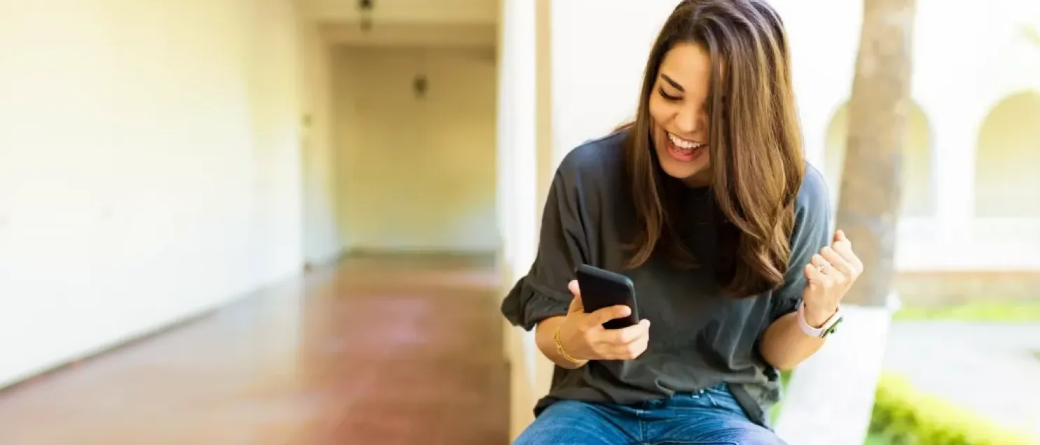 Persona celebrando mientras consulta información desde un teléfono móvil, destacando beneficios, gestión digital y acceso inmediato a servicios financieros.