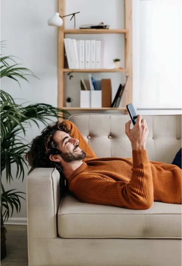 Persona utilizando un teléfono móvil desde la comodidad de su hogar para consultar información y gestionar servicios digitales.