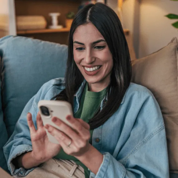 Una chica sentada en la sala de su casa mientras usa su celular.