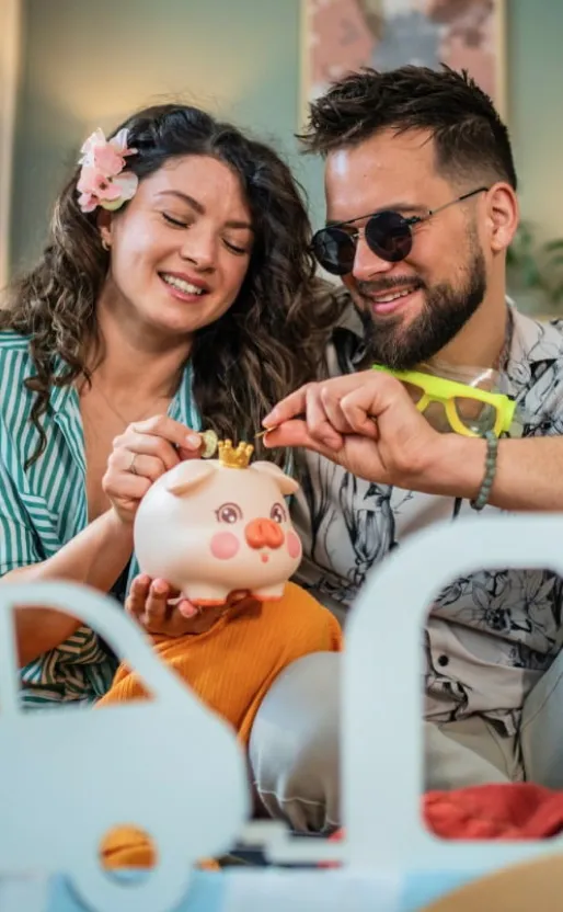 Pareja depositando monedas en una alcancía con forma de cerdito, representando el ahorro familiar, la planificación financiera y el cumplimiento de metas económicas con Banamex.