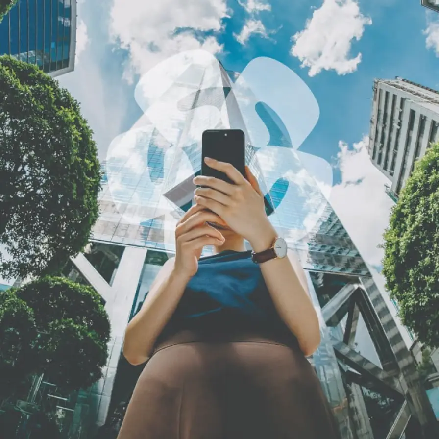 Persona utilizando un teléfono móvil frente a edificios corporativos modernos, representando la gestión digital de servicios financieros.