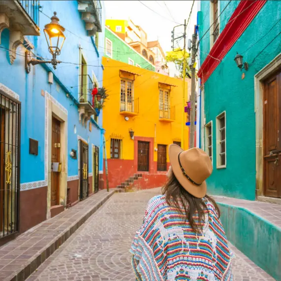 Persona recorriendo una calle empedrada con fachadas coloridas, rodeada de arquitectura colonial y colores vibrantes.