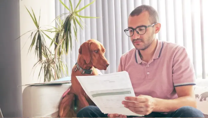 Persona revisando documentos financieros junto a su mascota en casa, para dar seguimiento a gastos, pagos y finanzas personales.