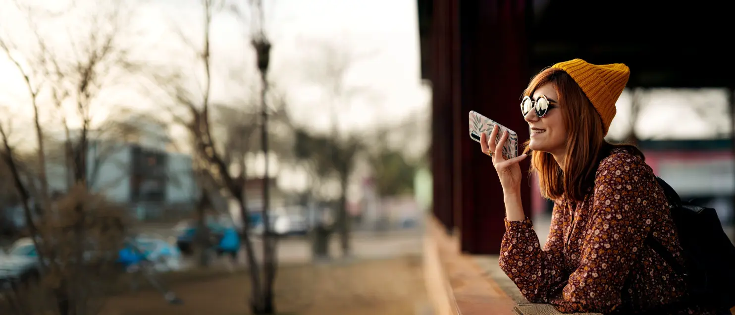 Persona utilizando un teléfono móvil al aire libre para comunicarse y gestionar servicios digitales mientras se desplaza por la ciudad.