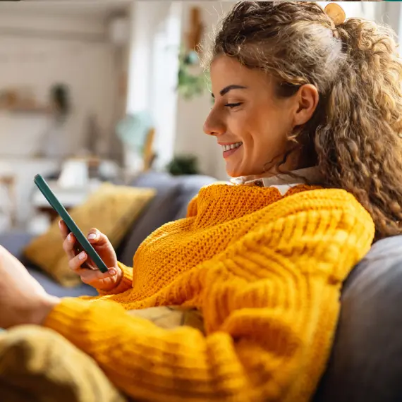 Persona consultando información financiera desde un teléfono móvil en casa, destacando comodidad, conectividad y gestión digital de servicios.