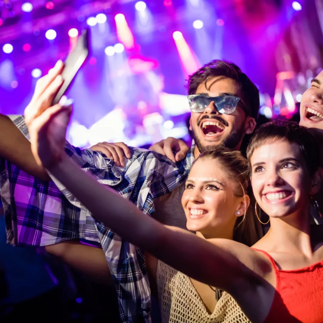 Un grupo de amigos tomandose una selfie en concierto con luces de escenario al fondo.