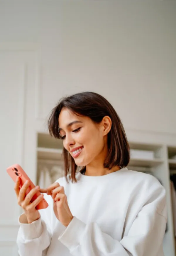Una mujer solicitando un crédito personal desde la app de su celular dentro de su cuarto.