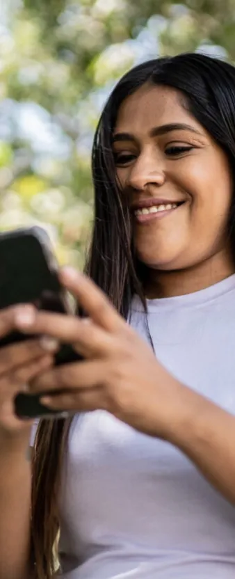 Una mujer sonriendo mientras ve su celular en un parque.