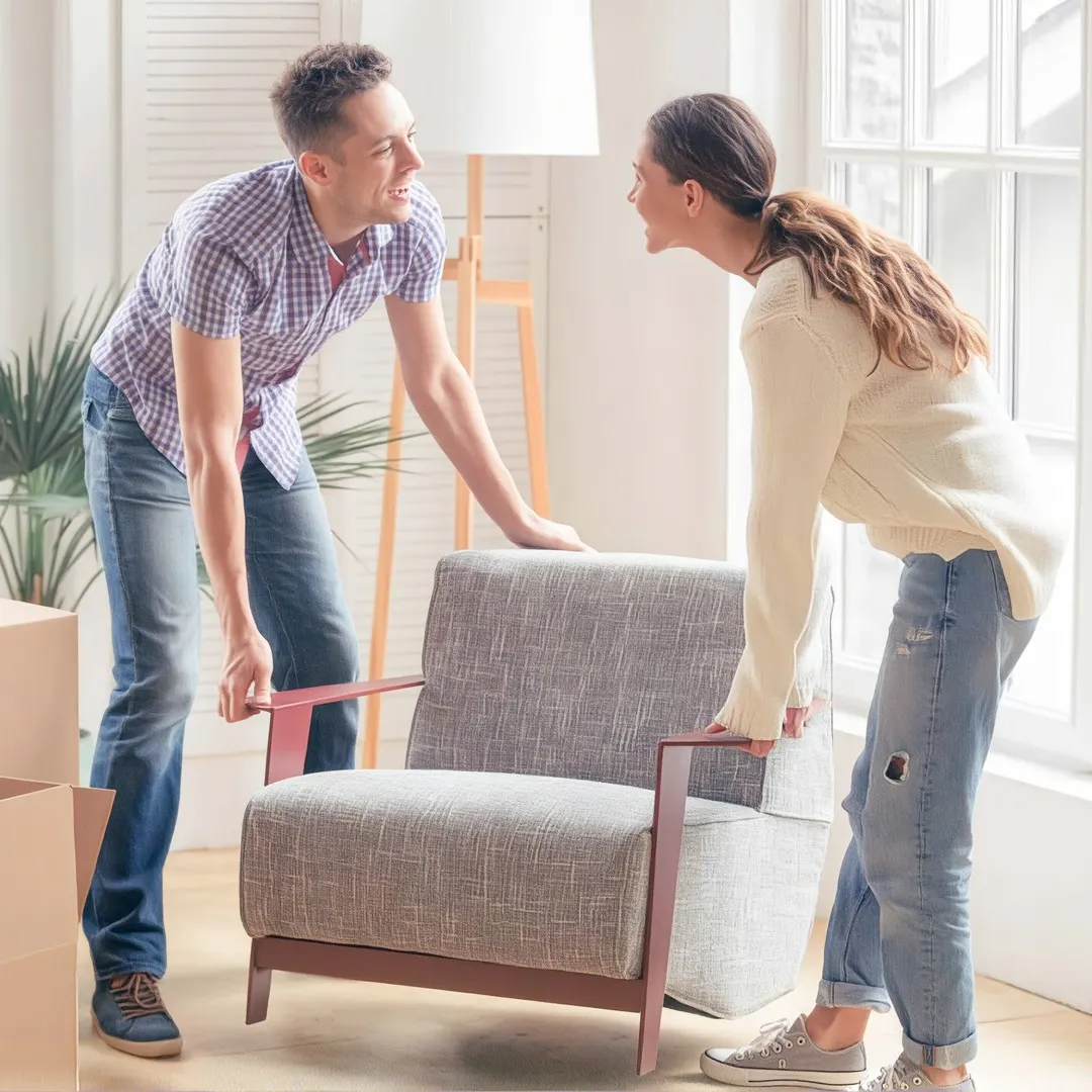 Personas acomodando un sillón dentro de una casa durante una mudanza con cajas alrededor.