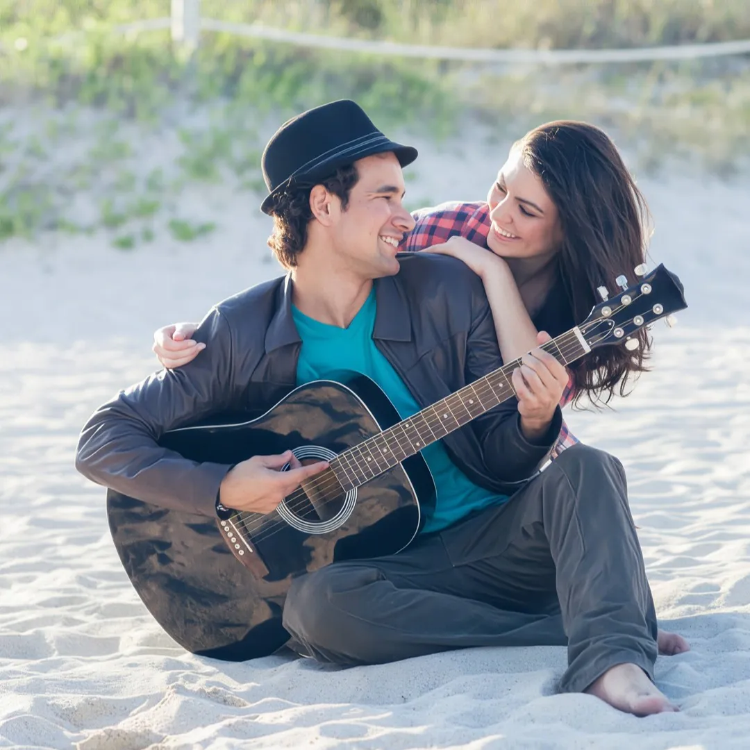Hombre toca la guitarra en la playa mientras su pareja lo abraza.