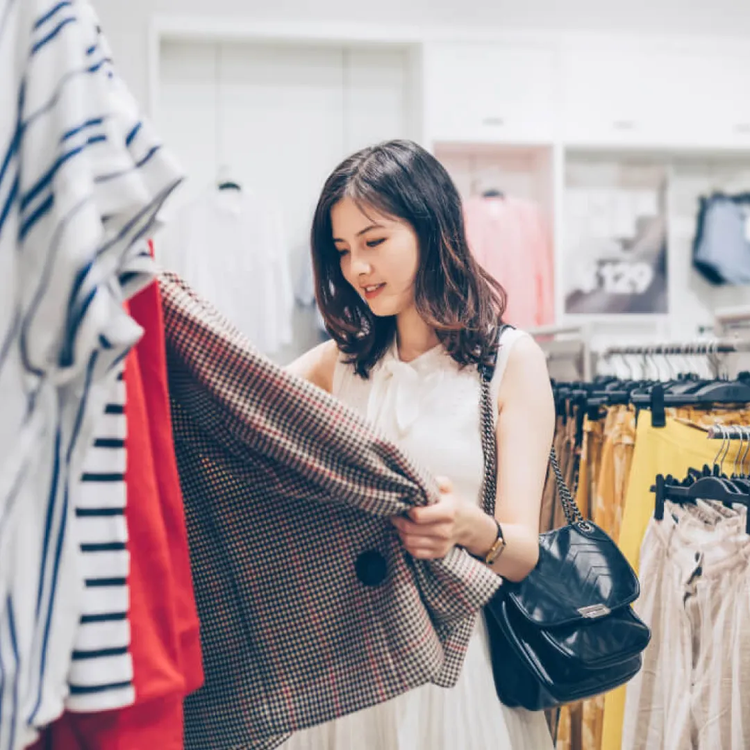 Persona eligiendo una prenda en un perchero dentro de una tienda de ropa.