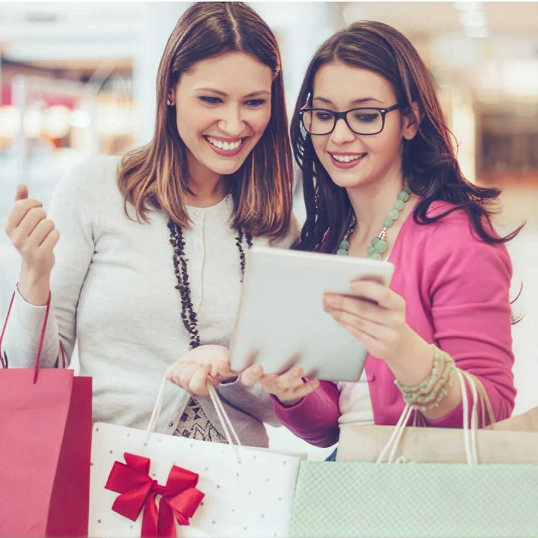  Dos mujeres sosteniendo sus bolsas de compras mientras revisan una tablet.