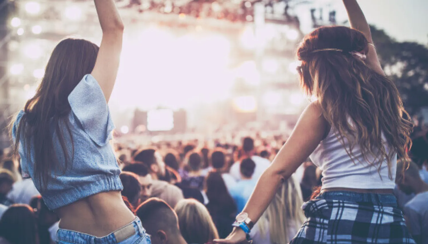  Un par de amigas disfrutando un concierto con los brazos arriba.