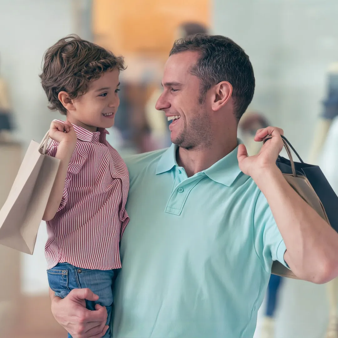 Padre e hijo sosteniendo bolsas de compras en un centro comercial mientras sonríen.