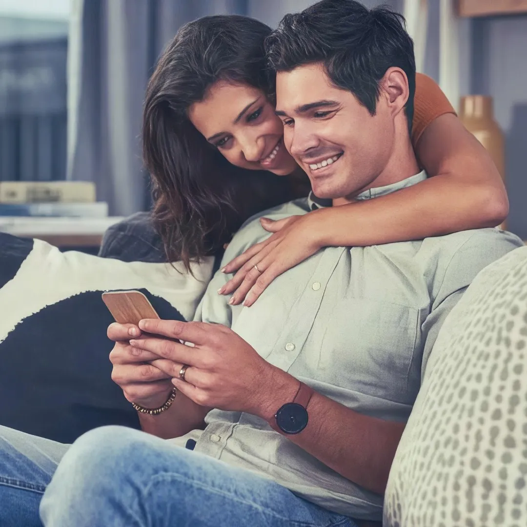 Una pareja sonríe mientras ven un celular en la sala.