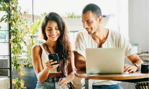 Una pareja revisando la App Banamex en el celular de ella, frente a su laptop.