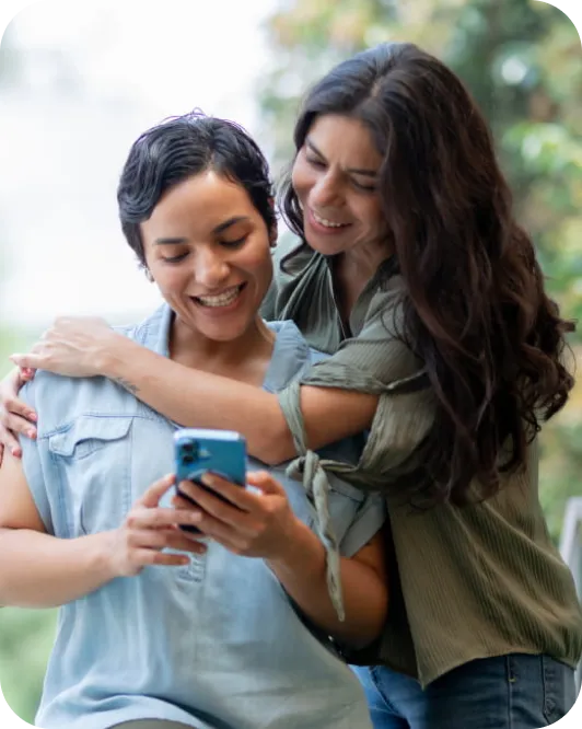 Un par de amigas abrazadas mientras una sostiene su celular.