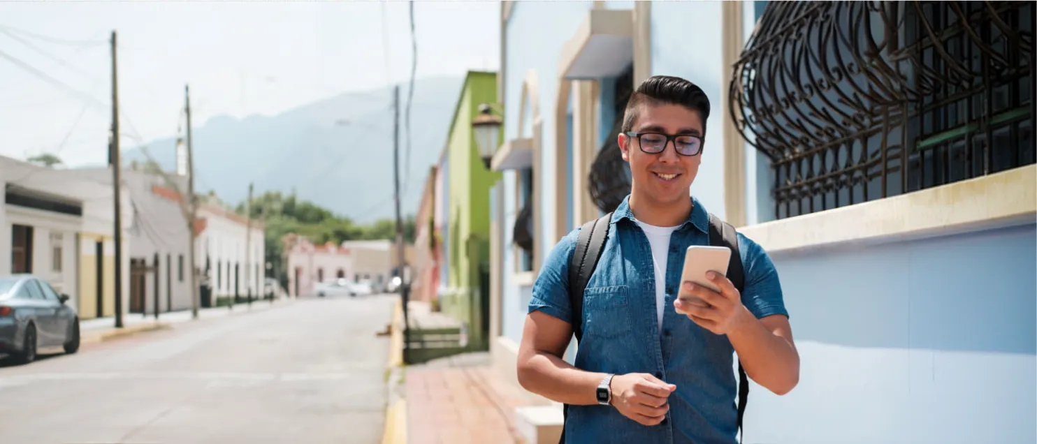 Un hombre caminando por una calle mientras consulta su celular.