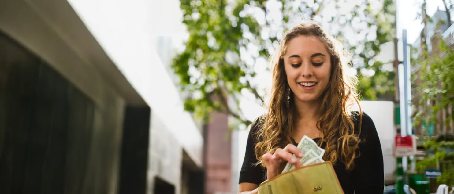 Una mujer sacando billetes de su cartera mientras va caminando por la calle.