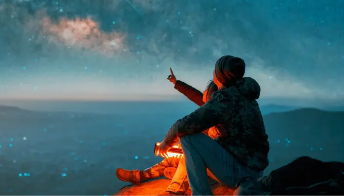 Persona observando el cielo estrellado desde una montaña durante la noche, destacando naturaleza, contemplación y paisajes nocturnos.