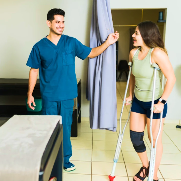 Persona en proceso de recuperación física utilizando muletas, acompañada por un profesional de la salud durante una sesión de rehabilitación.