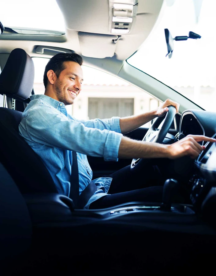 Persona conduciendo un automóvil mientras interactúa con la pantalla del vehículo, representando protección y seguridad durante los trayectos.