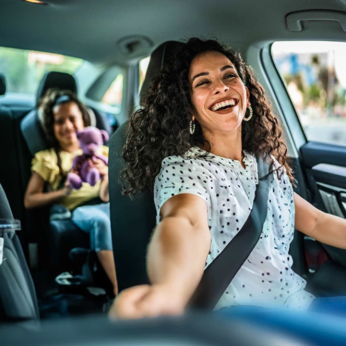 Persona conduciendo un automóvil acompañada por un menor en el asiento trasero, representando protección y seguridad durante los traslados familiares.